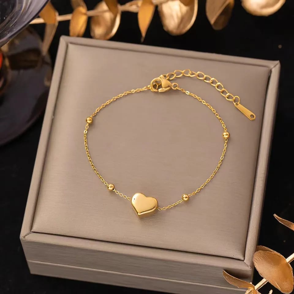 Gold bracelet with a heart charm on a gray jewelry box
