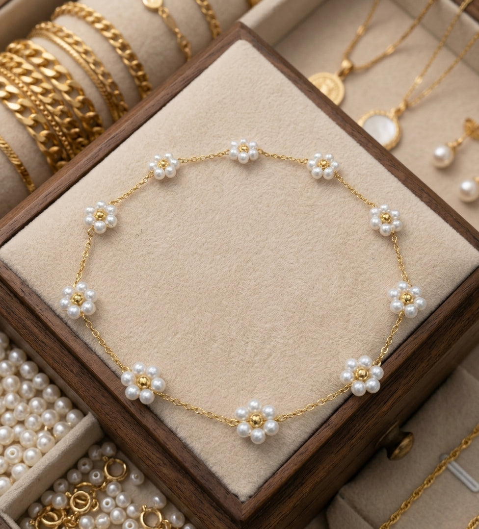 A gold chain bracelet decorated with nine white pearl flower motifs, displayed on a beige velvet-lined wooden jewelry box.