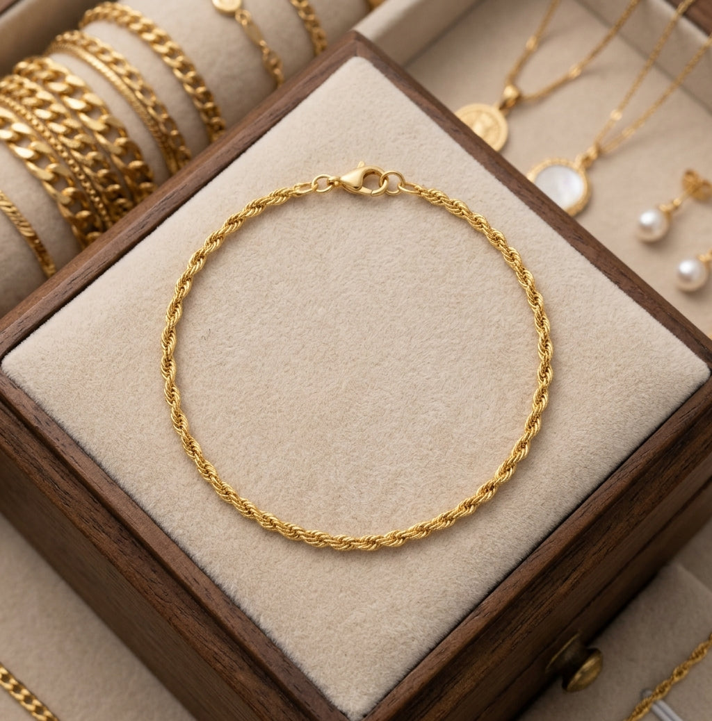 A gold rope-style bracelet displayed on a beige velvet-lined jewelry box, with additional gold jewelry visible in the background.