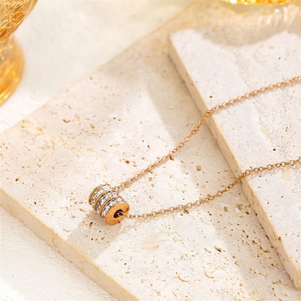 Gold necklace with a cylindrical pendant on a textured beige surface
