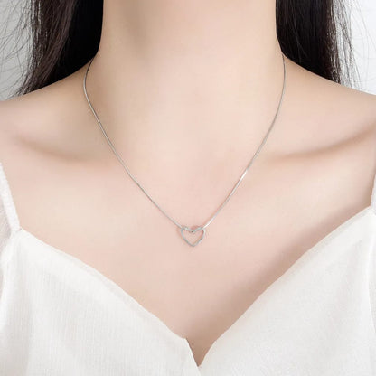 Silver necklace with a heart pendant worn by a person on a white background