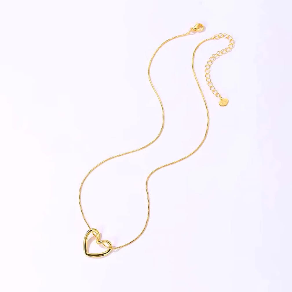 A delicate gold chain necklace featuring a small open heart pendant at the center, with an adjustable chain extension and a small heart charm, displayed on a clean white background.
