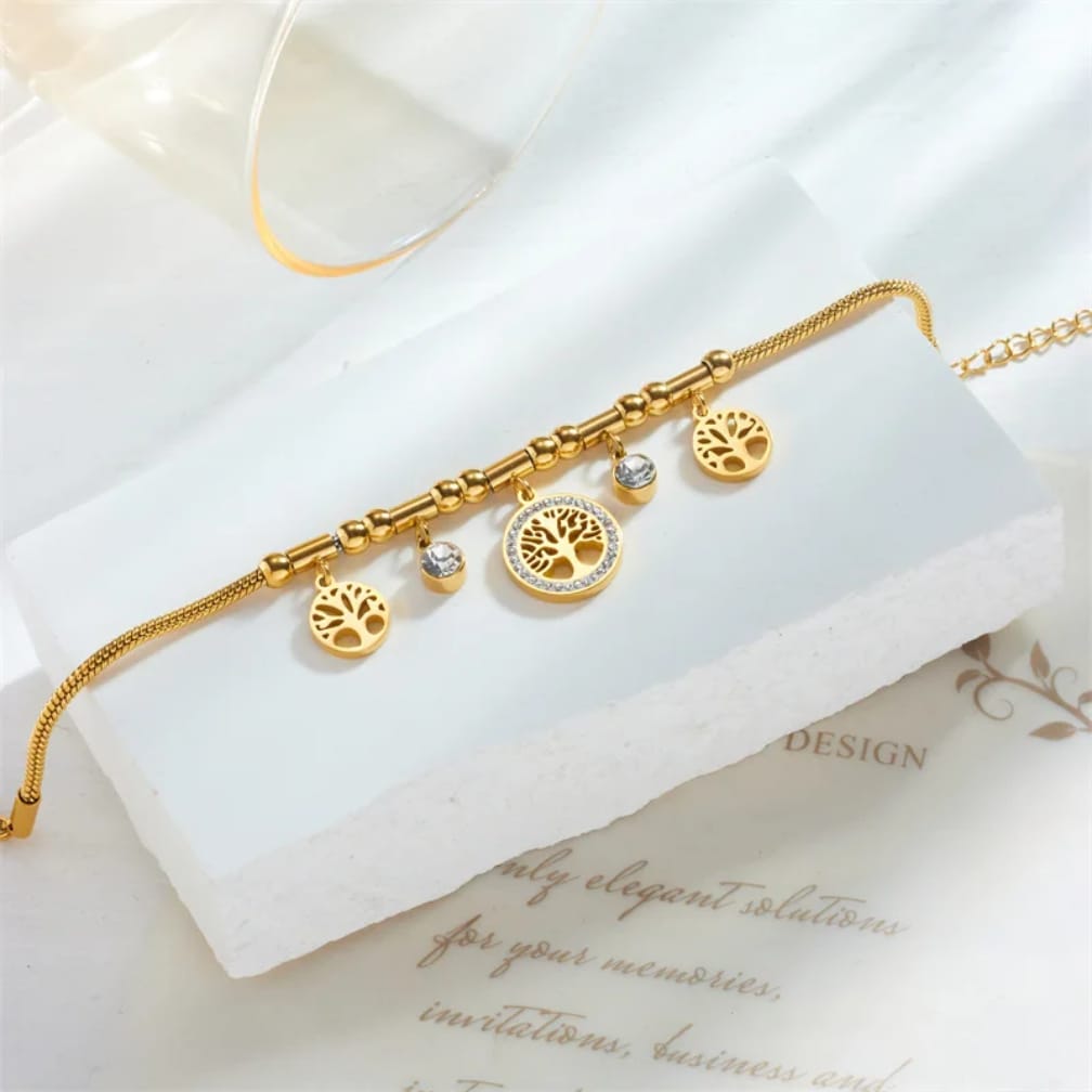 Gold bracelet with tree-shaped charms on a white surface