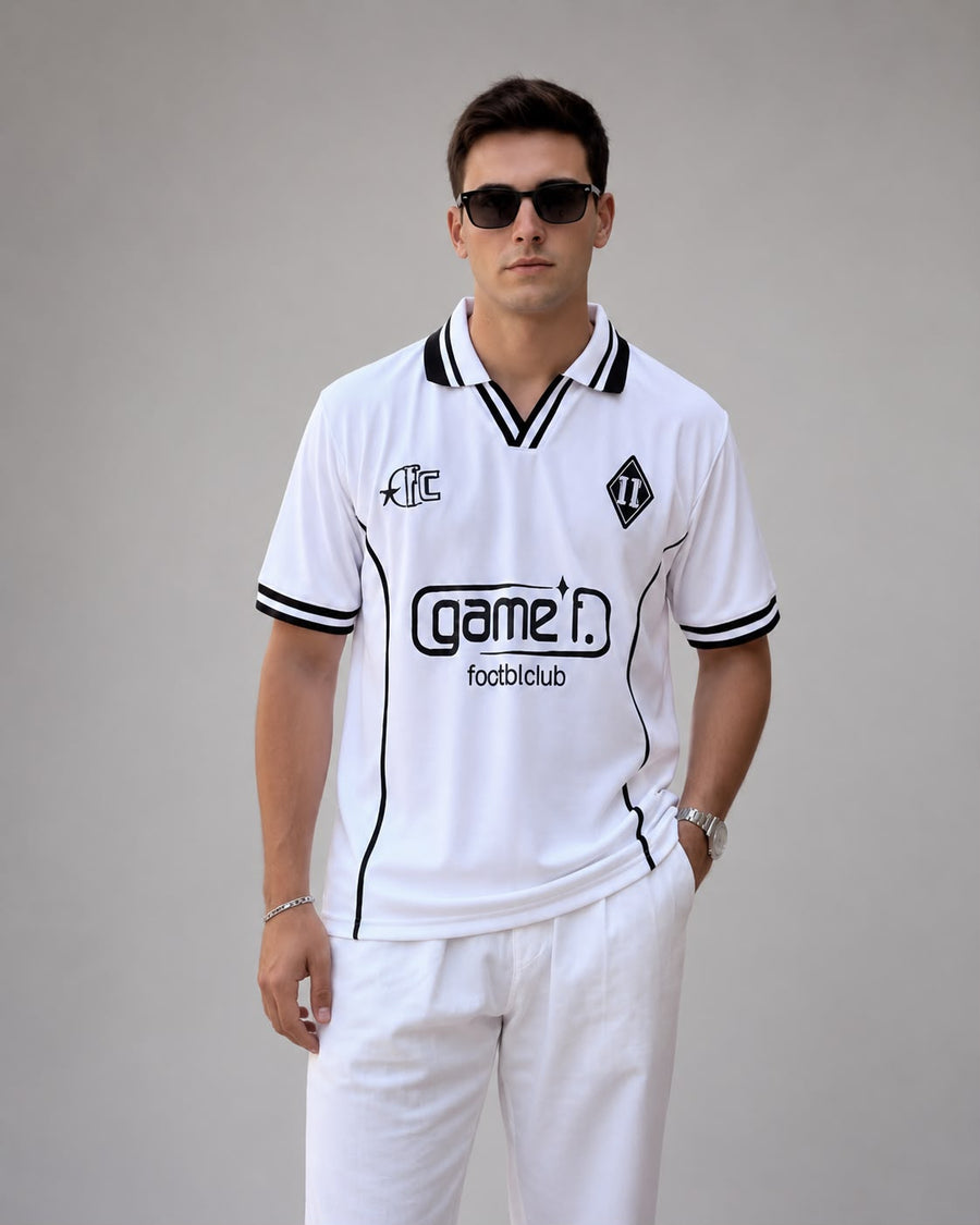 A man modeling a white short-sleeve sports jersey with black trim, featuring the 'Game i. footbloblub' logo on the chest, set against a plain gray studio background.