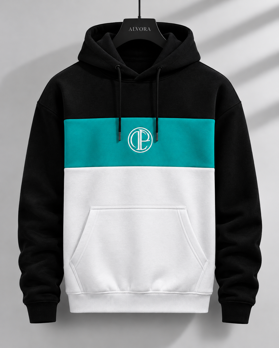 A color-blocked pullover hoodie hanging on a black hanger against a light gray wall with soft diagonal shadows. The hoodie has a black upper section and sleeves, a teal middle band with a white circular 'CP' monogram logo, and a white lower section.