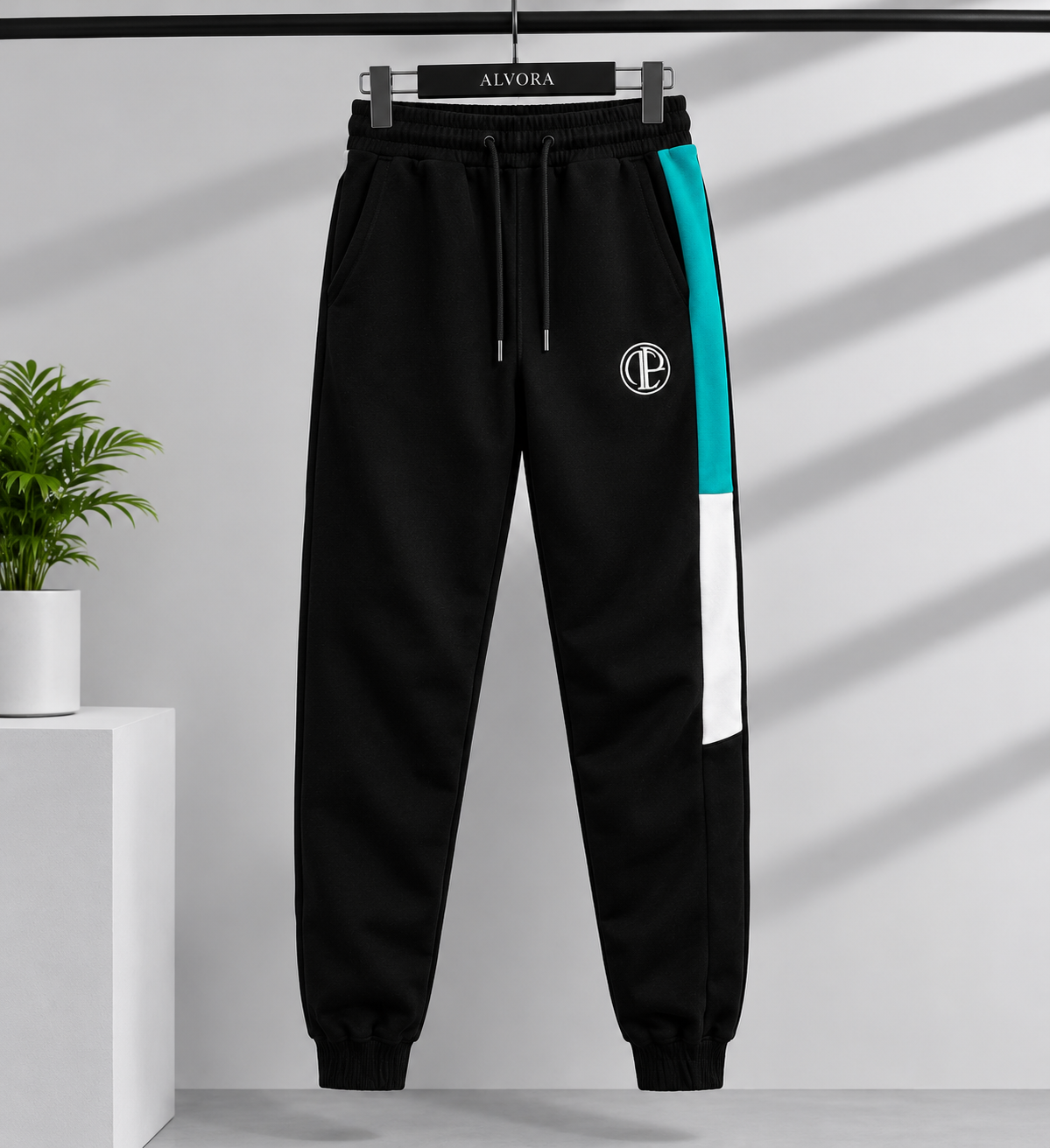 Black jogger sweatpants with a teal and white side stripe, a white circular 'EC' logo on the upper left thigh, and a black drawstring waist, hanging on a black hanger labeled 'ALVORA' against a light gray wall with diagonal shadows.