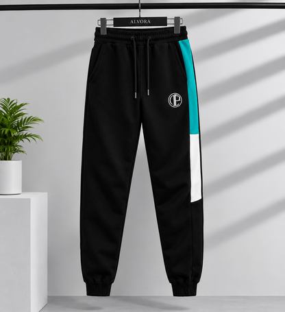 Black jogger sweatpants with a teal and white side stripe, a white circular 'EC' logo on the upper left thigh, and a black drawstring waist, hanging on a black hanger labeled 'ALVORA' against a light gray wall with diagonal shadows.