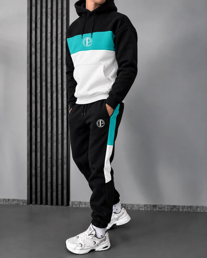 A person modeling a black, white, and teal color-block hoodie and matching sweatpants with a circular 'P' logo on the chest and thigh, paired with white sneakers, set against a gray studio background with a vertical slatted panel.